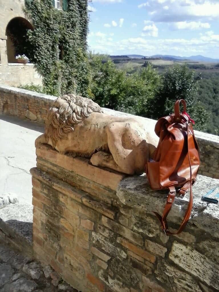 Un leone di pietra addormentato su un muretto, accanto a uno zaino di cuoio