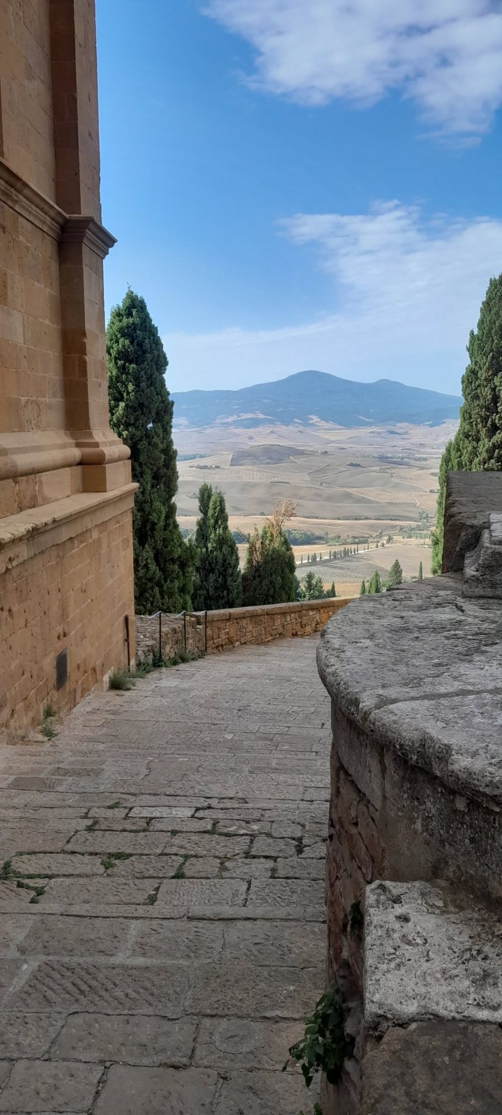 Una strada lastricata fra le mura e i cipressi, aperta sulla Val d’Orcia